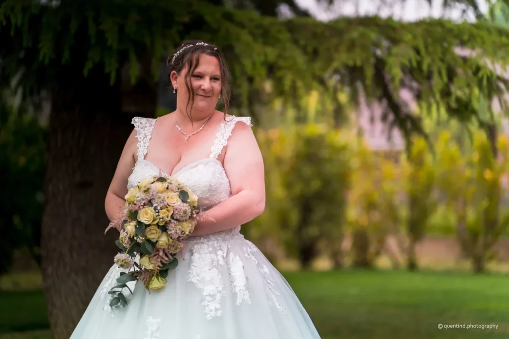 Portrait élégant de mariée en robe de dentelle blanche tenant son bouquet de roses