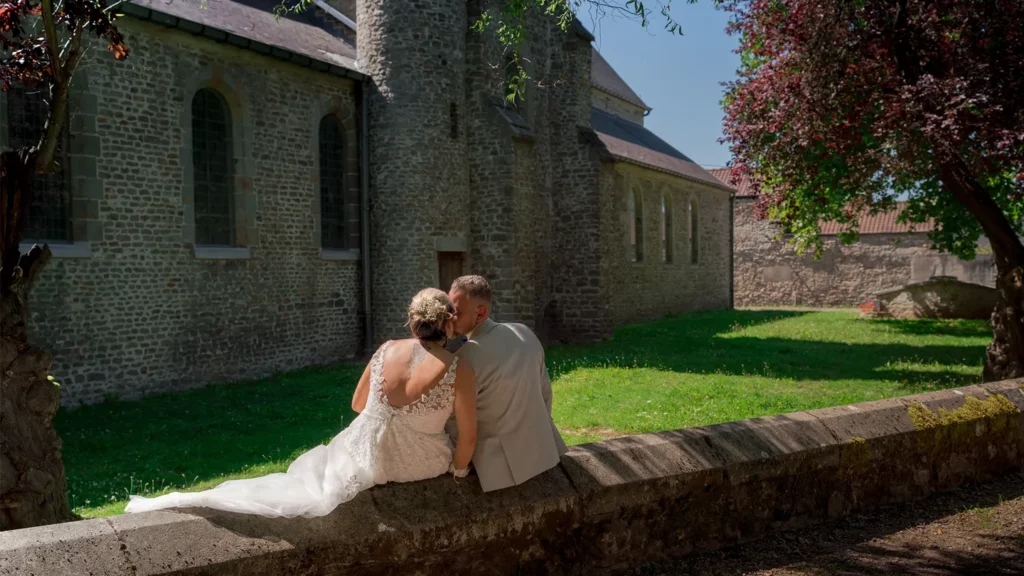 Jeune couple assis sur un muret près d'une vieille église en pierre.